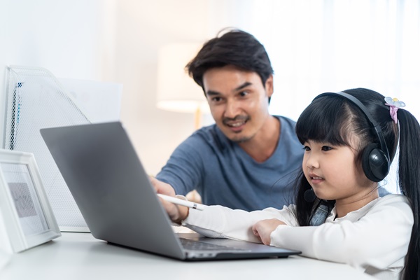 Asian little young girl kid learning online class at home with father.